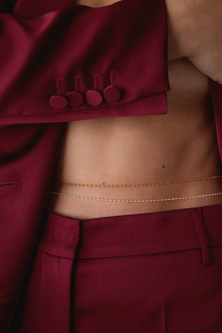 Woman wearing a burgundy blazer open to show her belly showing layed 14k gold-fill and sterling silver belly chains