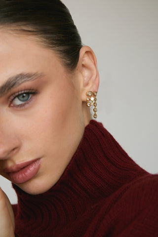 Woman looking into the camera, wearing a red turtleneck and 14k gold-filled earrings with white sapphire accents. 