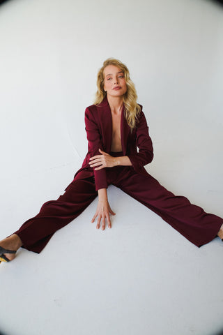 Woman wearing a burgundy suit and 14k gold-filled hand chains sitting on the floor against a white background.