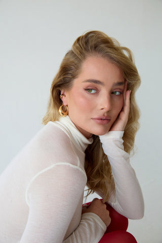 Woman wearing a white turtleneck, red tights, ac hunky 14k gold-filled ehoop and 14k gold vermeil ear cuff. 