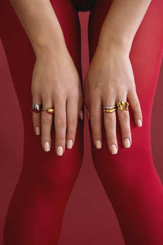 Woman wearing red tights with her hands on her knees showing multiple stacked rings made of sterling silver and 14k gold-fill.