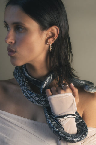 Woman wearing gold bezel drop earrings, and ear cuff and gold earring holding a snake with a neutral background