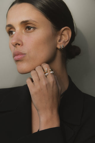 Woman wearing gold earrings and a ring set  against a neutral background