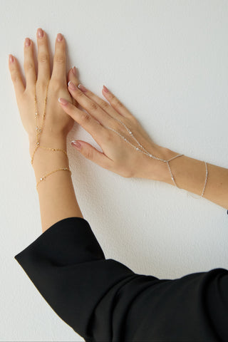 Close-up of gold and silver hand chains worn on hands against a white wall