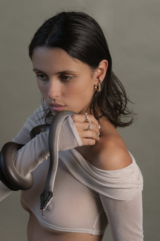 Woman wearing gold earrings and gold and silver rings holding a snake against a neutral background