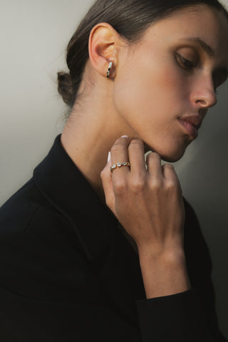 Close-up of a woman wearing earrings and a ring, with a neutral background