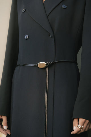 Close-up of a black coat with a black leather corded belt with gold buckle accent and buttons on a neutral background