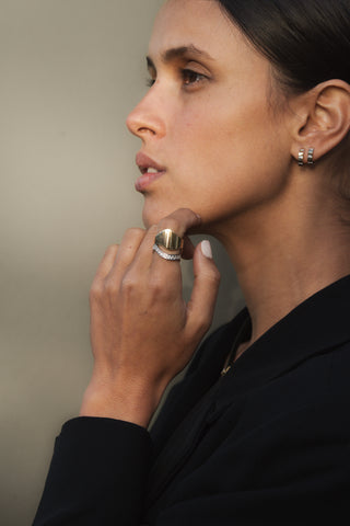 Woman wearing a gold ring and earrings against a neutral background