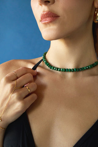 Close-up of a person wearing a green beaded necklace against a blue background