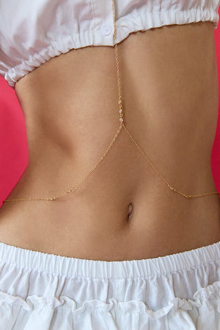 Gold body chain worn by a person with white shorts on a pink background