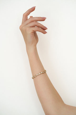 Hand casually pointed upward wearing a gold tennis bracelet with lab grown white sapphires against a plain background