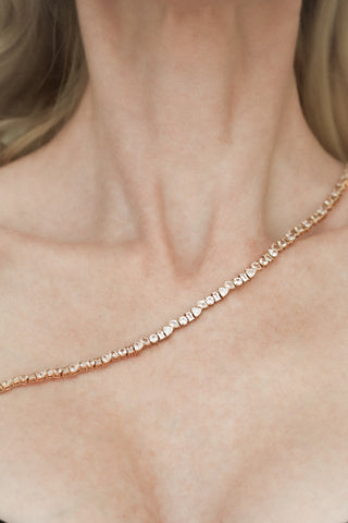 A gold tennis necklace with alternating cuts of trillion, round, pear, and baguette diamonds draped across a woman's décolletage.