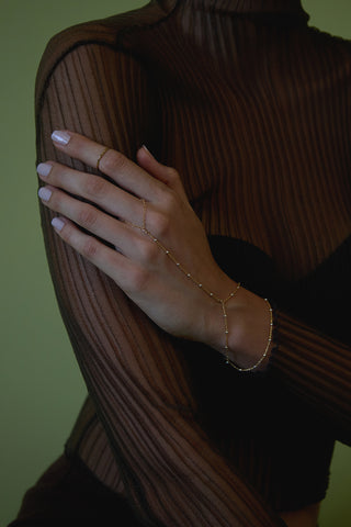 A person's hand wearing a gold hand chain with small silver beads.