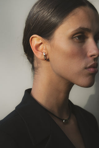Close-up of a person wearing earrings  and a cord necklace with pendant with a neutral background