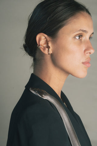 Woman wearing a gold ear cuff and earring with white sapphires in a black blazer with a snakes slithering over her shoulder against a plain background.