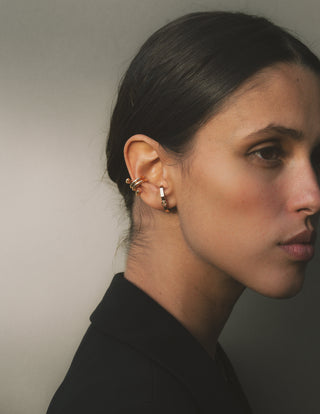 Close-up of a woman wearing gold earrings and gold ear cuff against a neutral background