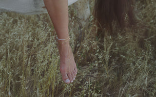 A foot with a gold and pearl anklet and gold foot chain hanging off the side of a horse in a field