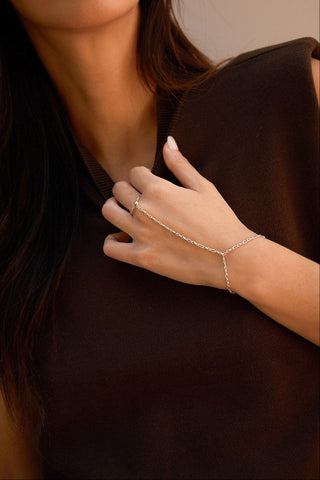 A close-up of a model wearing a delicate  mixed metal hand chain, styled with a dark brown sleeveless top.