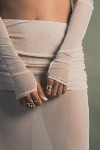 Close-up of a person wearing ring stacks and ring sets in gold and silver in a sheer white shirt and a matching dress against a blurred background.