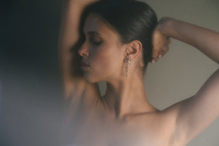 Woman with a blurred background, wearing bezel set tennis drop earrings in 14k gold vermeil with white sapphires.