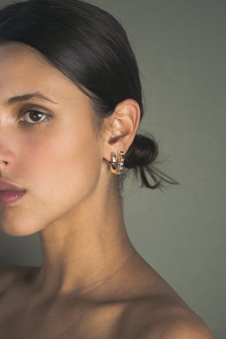 Close-up of a woman wearing a gold huggie and hoop earrings with white sapphire accents with a neutral background