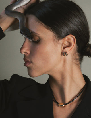Woman with a snake on her head wearing earrings and a cord necklace.