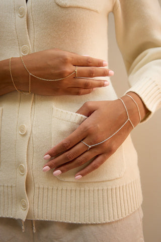 A close-up of a person wearing delicate gold chain hand, styled with a cream-colored knit cardigan.