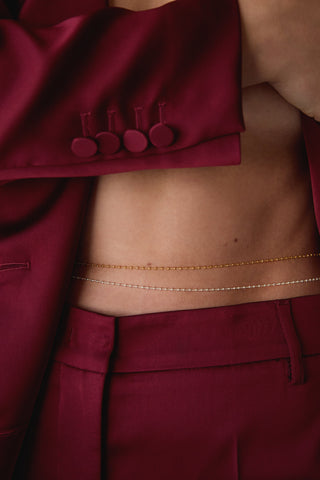 Close-up of a person wearing a burgundy outfit with layered gold and silver belly chains.