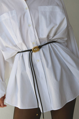 White shirt with a belt and gold sculptural buckle on a plain background