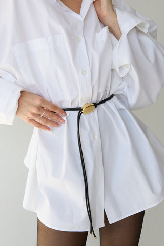 Person wearing a white oversized shirt with a black belt and gold buckle.