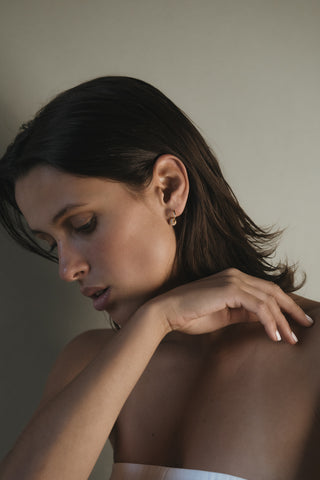 Woman with wearing a gold hoop with hand on shoulder against a neutral background