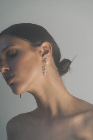 Close-up of a woman wearing gold tennis bezel earrings against a neutral background
