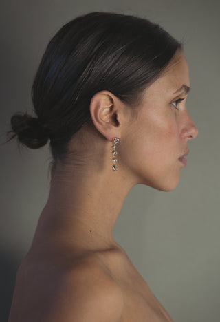 Side profile of a woman wearing tennis drop earrings against a neutral background