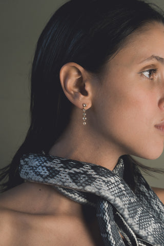 Close-up of a woman wearing bezel set gold drop earrings with a snake around her neck.