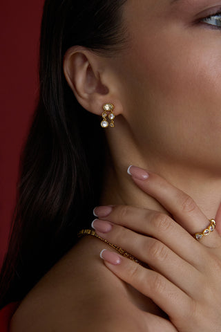Close-up of a woman wearing gold earrings and a ring with a red background