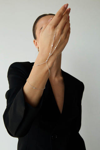 Person wearing a delicate silver hand chain and black blazer on a plain background