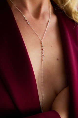 Close-up of a person wearing a delicate body chain with colored gemstones with a red suit on