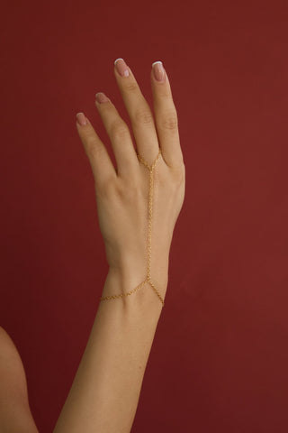 Thin, delicate, gold hand chain on a hand against a red background