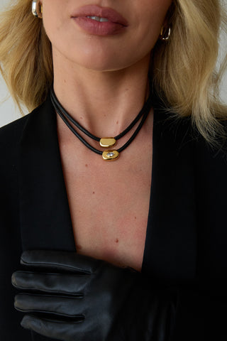 Close-up of a person wearing a black leather necklaces with gold pendants.