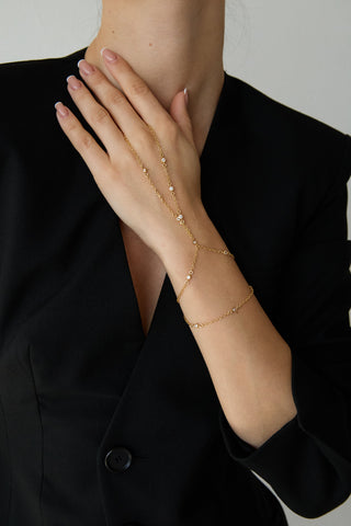 Person wearing a delicate gold hand chain and black blazer on a plain background