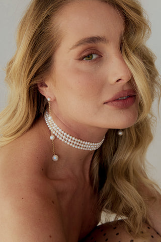 Woman wearing a pearl necklace and earrings against a neutral background