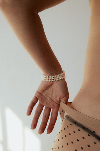 Hand wearing a pearl bracelet on a neutral background