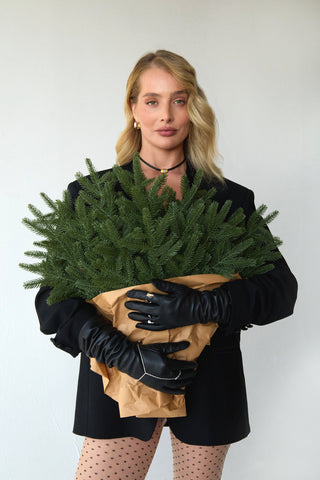Woman wearing a black cord necklace and black leather gloves holding a bundle of christmas tree branches against a white background 