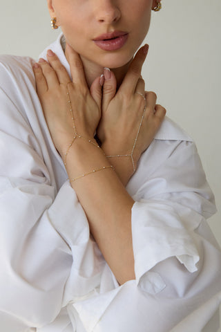 Close-up of a woman wearing a delicate gold hand chain on a plain background