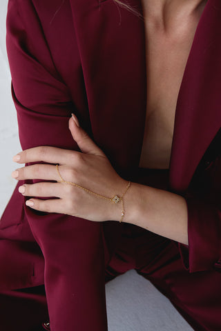 Person wearing a burgundy suit with a gold hand chain on a neutral background