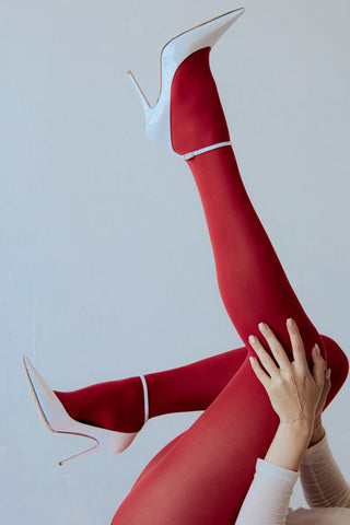 Woman wearing a gold hand chain with pearl accents, Red tights and white high heels on a plain background