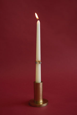 White candle in a bronze holder on a red background with rings stacked on the candle stick