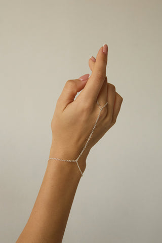 Hand wearing a delicate silver hand chain against a neutral background
